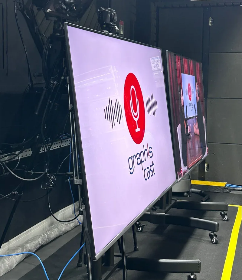 Telões exibindo a identidade visual do GraphisCast nos bastidores do estúdio